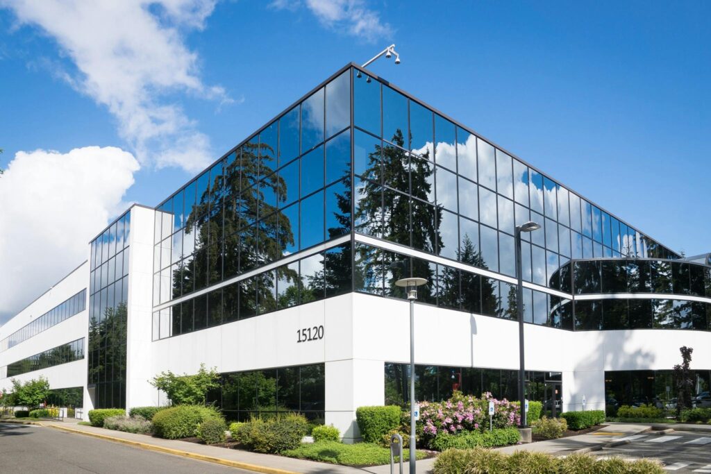 Glass-front office building with maintained shrub beds and lawn at the entrance