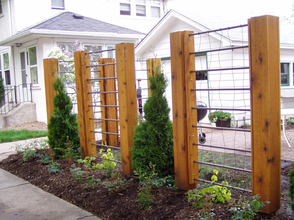 Cedar post trellis screen with evergreens and a mulch bed at a commercial entrance