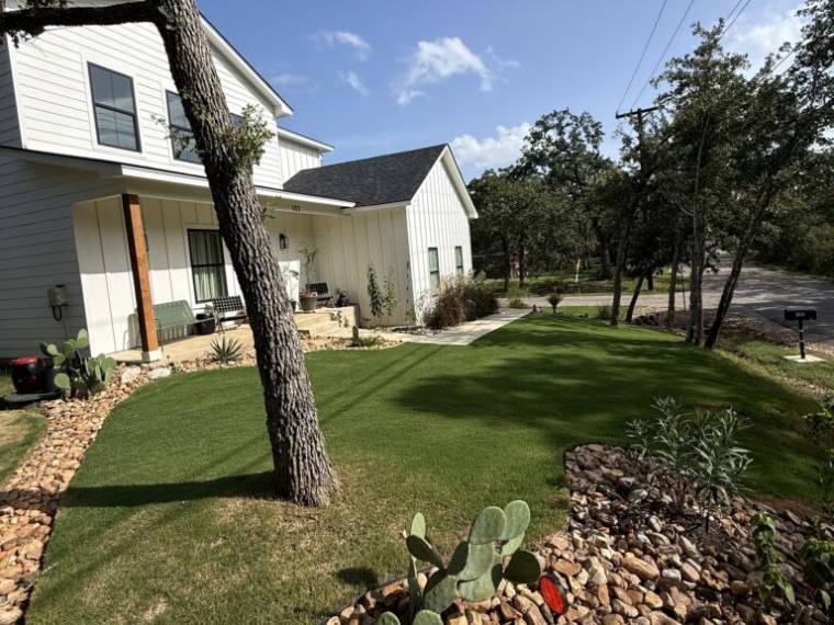 Lawn and rock bed with prickly pear framing a farmhouse under the Lost Pines